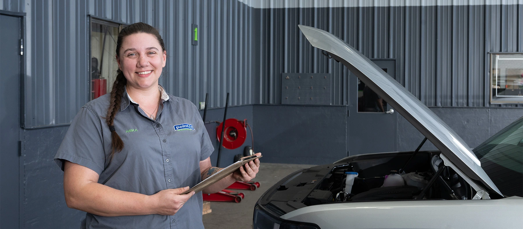 A Point S service advisor holding an inspection clipboard beside a vehicle with its hood raised