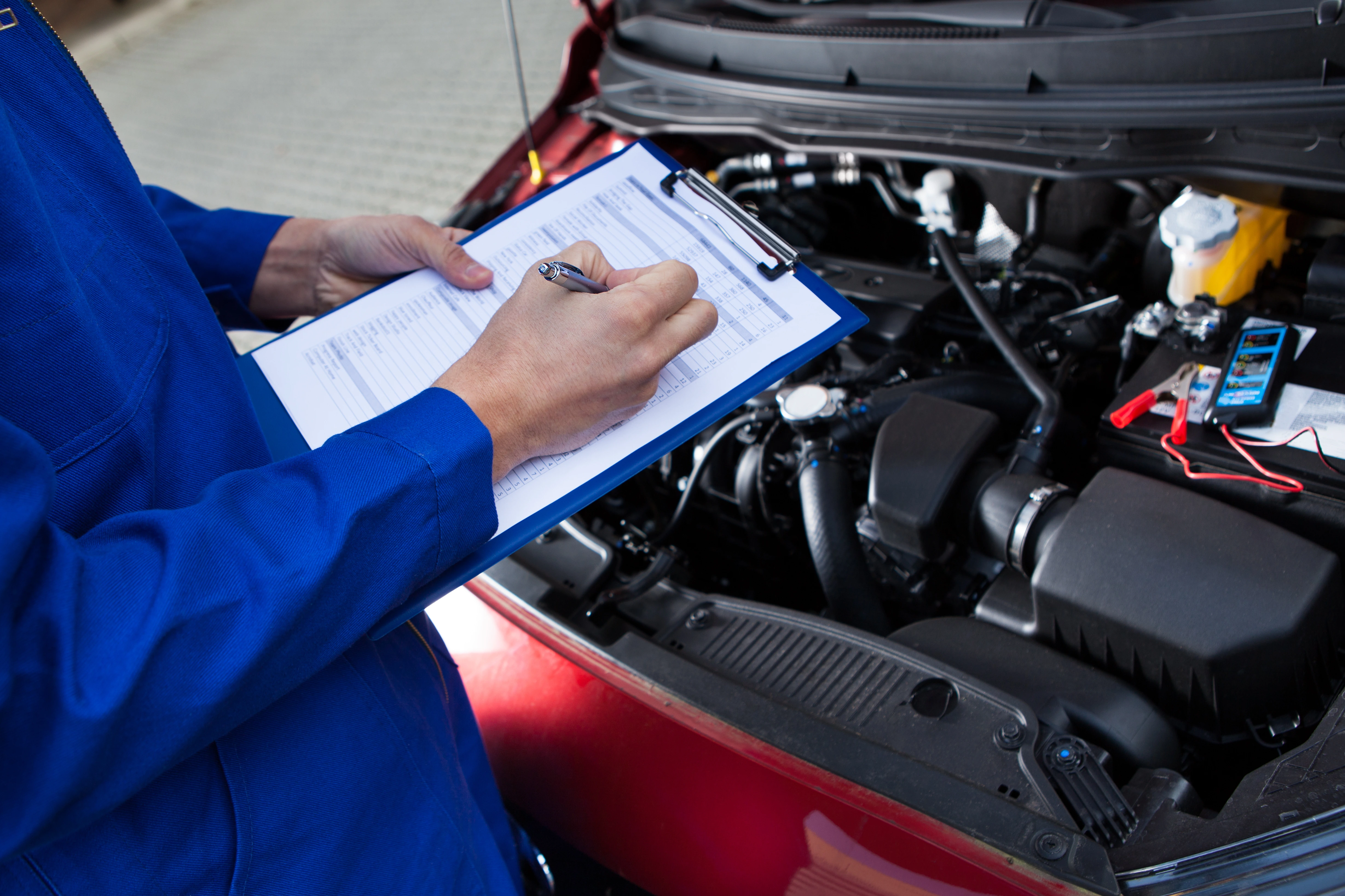 Mechanic inspecting vehicle engine with clipboard